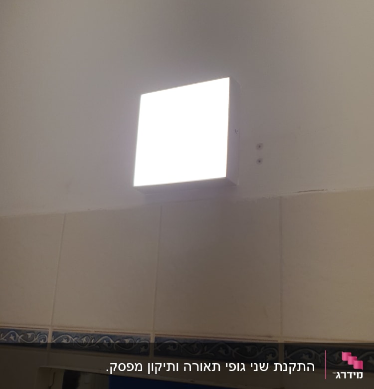 מנורת קיר מרובעת מוארת על קיר לבן